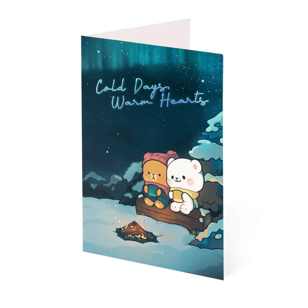 Greeting card with Milk and Mocha by a campfire under a starry winter aurora. 'Cold Days, Warm Hearts'.